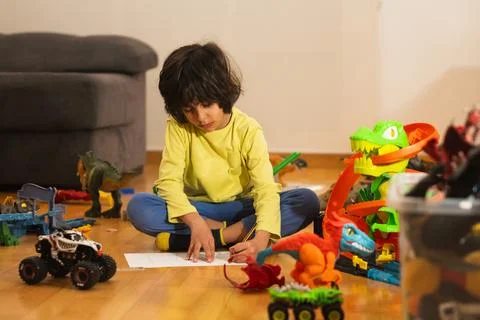 Young boy drawing on paper while playing with toys Stock Photos