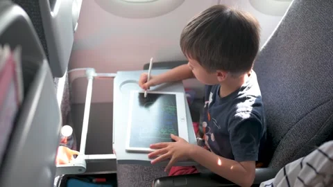 Young boy drawing on tablet in airplane seat with natural light Видео 337788468