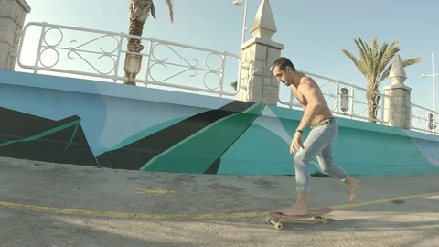 Young boy dressed in jeans without t-shirt skating barefoot along the seaside Stock Footage 141677647
