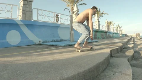 Young boy dressed in jeans without t-shirt skating barefoot along the seaside Stock Footage 141677924