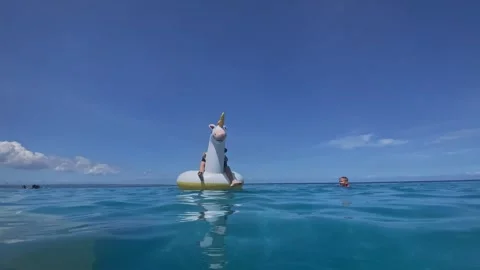 Young boy drifts on unicorn float over tranquil ocean surface Stock-Footage 335713010