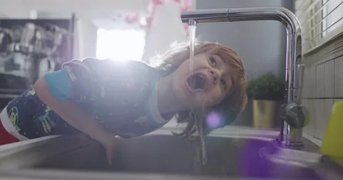 Young boy drinking water directly from kitchen sink tap in daylight Stock Footage 274934666