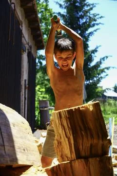 Young boy driving axe into large log while preparing firewood outdoors 스톡 사진