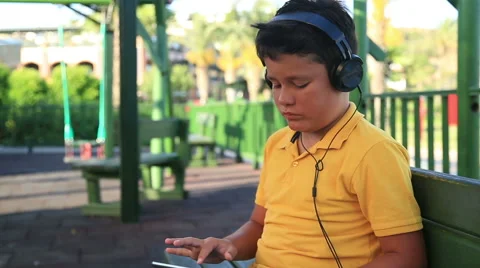 Young boy with  earphone using digital tablet at the park 2 Stock Footage 64804549
