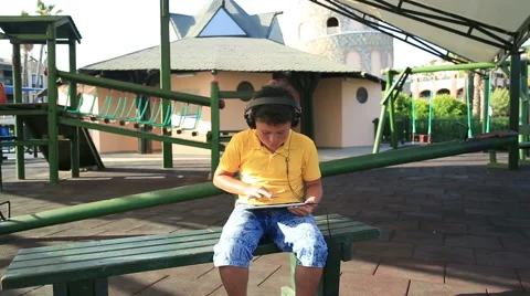 Young boy with  earphone using digital tablet at the park Vídeo Stock 64804768
