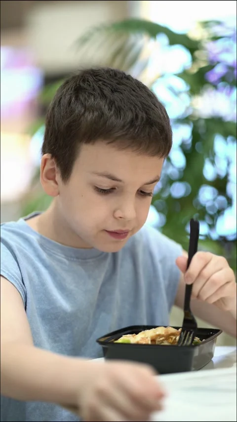 Young boy eating fresh Caesar salad at a food court, enjoying a healthy lunch Video stock 343157477