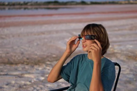 Young boy in eclipse glasses gazes up in wonder during a solar eclipse from.. Stock Photos