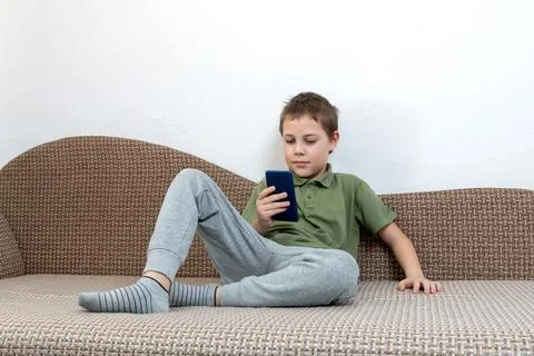 A young boy, engrossed in a digital device, sits comfortably on the couch. .. Stock Photos