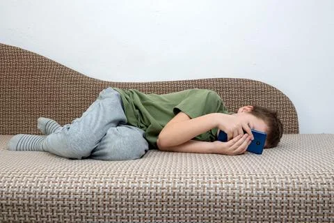 A young boy, engrossed in a digital device, sits comfortably on the couch. .. Stock Photos