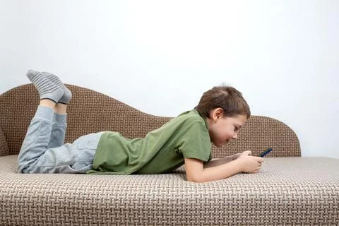 A young boy, engrossed in a digital device, sits comfortably on the couch. .. Stock Photos