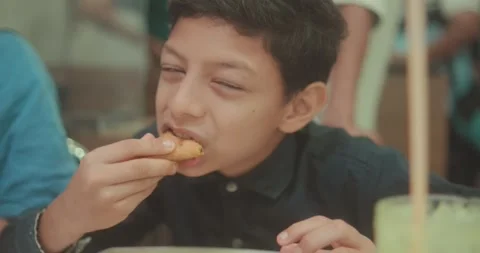 Young boy enjoying a meal at a table in a warm casual setting, capturing Stock Footage 336000097