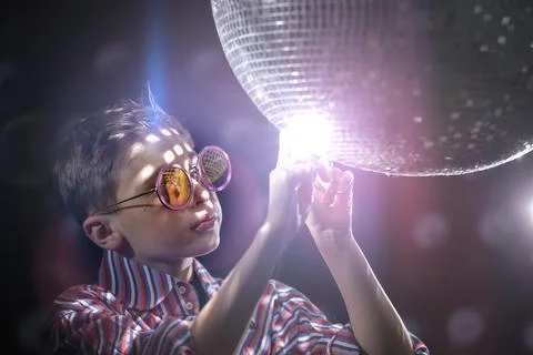 A young boy at an evening party in the rays of light and with a disco ball. Stock Photos