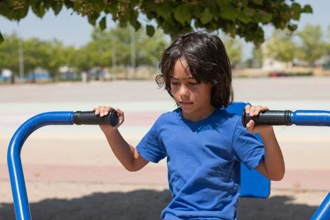 Young boy exercising on a blue machine in an outdoor gym Foto stock