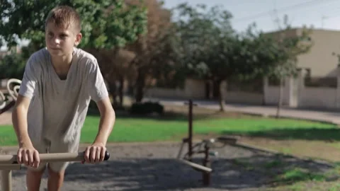 Young Boy is exercising outdoors. He is using the parallel bars at a calist.. Video stock 294550154