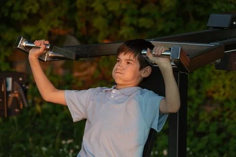 Young boy exercising on a weightlifting machine outdoors in a garden settin.. Stock Photos