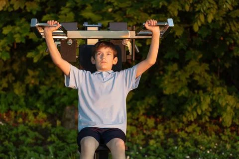 Young boy exercising with weights on a strength training machine outdoors, .. Stock Photos