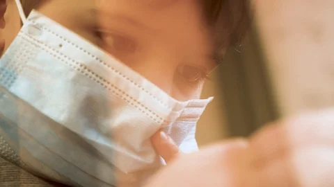 Young boy in face mask playing game on mobile phone. Kid sitting on windowsill Stock Footage 129062427