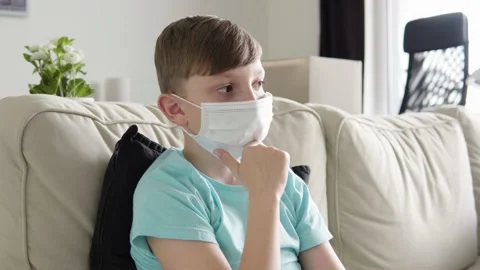 A young boy in a face mask thinks about something as he sits on a couch at home Stock Footage 138167669