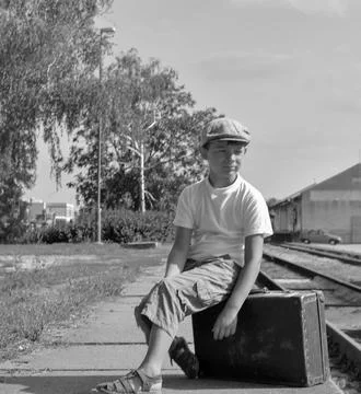 Young boy in flat cap sits on vintage suitcase at train station platform Stock-Fotos