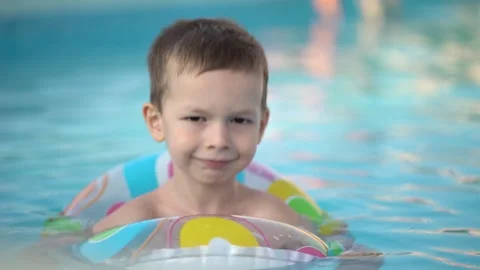 Young boy floating peacefully with a big smile in a colorful donut ring  Video stock 342272152