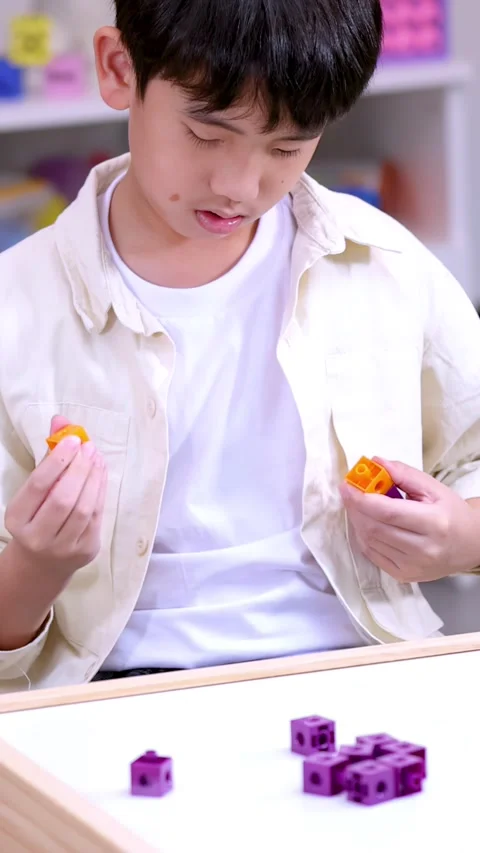 Young Boy Focused on Connecting Colorful Math Manipulative Cubes in Classroom Stock Footage 324934436