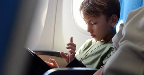 Young boy focused on educational game on tablet during flight Stock Footage 303994314