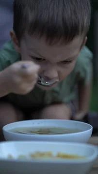 Young boy with focused expression eats soup from white bowl using metal spoon 写真素材