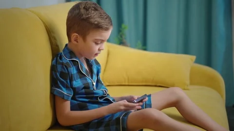 Young boy focused on smartphone while relaxing on yellow couch Stock Footage 303804429