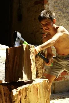 Young boy forcing splitting axe through large log outdoors 스톡 사진