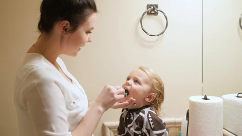 Young boy gets help from young mom brushing his teeth in the bathroom Stock Footage 86712194