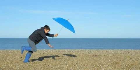 A young Boy getting blown along a beach by strong winds. Video stock 86423433