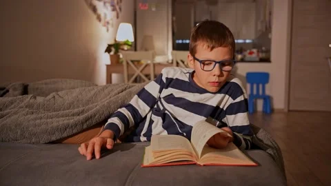 Young boy with glasses reading book while relaxing Stock Footage 297904379