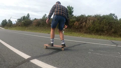 Young boy gliding with a longboard down the road Stock Footage 141085442