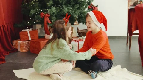 A young boy hands Christmas present teddy bear to a girl, sitting joyfully by Stock Footage 290464460