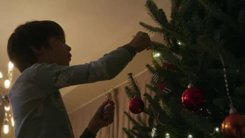 Young boy hanging up reusable tinsel on indoor christmas tree at night prep.. Stock Footage 345535211
