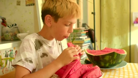 Young boy happily eats refreshing watermelon in cheerful kitchen setting Stock-Footage 321028723
