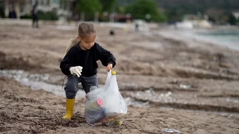 Young boy happily picking up trash on beach, people in nature Stock Footage 285590900