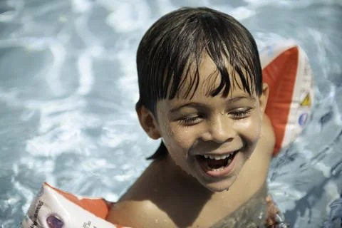 Young boy happily smiling in pool with water wings on Stock Photos