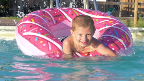 Young boy has fun in the pool by swimming on an inflatable donut 動画素材 139211478