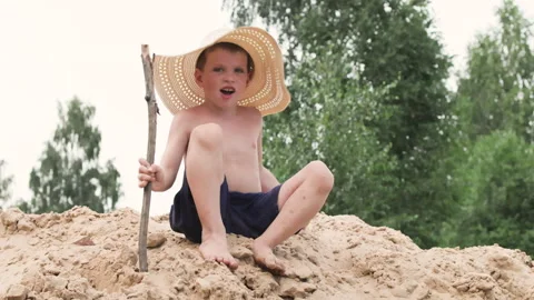 Young boy in hat conquers sandy hill while holding stick in summer adventure. Stock Footage 287680088