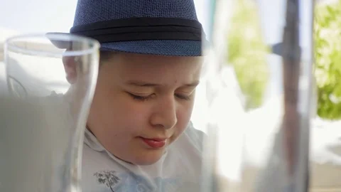 Young boy with hat sitting under umbrella using smartphone and drinking soda Stock Footage 84390859