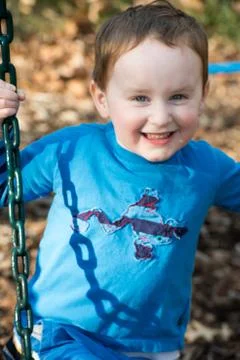 Young boy having fun outside at park on a playground swing set Stock Photos