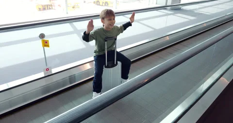 Young boy having fun sitting his suitcase on moving walkway at airport Stock Footage 304071873