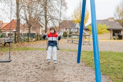 Young boy having fun swinging in playground outdoors Stock Photos