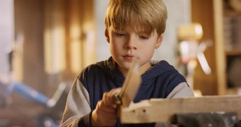 Young boy in his dad's workshop is sawing a wooden plank Stock Footage 85809183