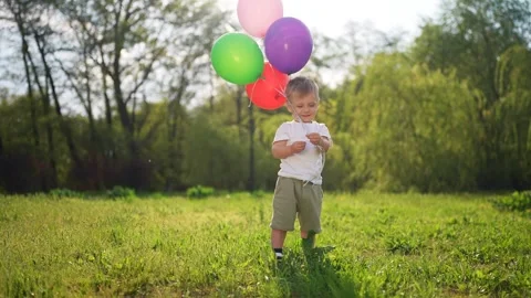 Young boy holding bunch of balloons. Child holding balloons in the summer. A Video stock 320472300