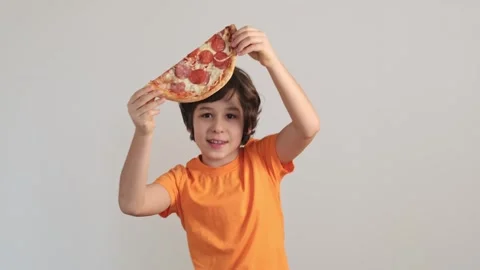 A young boy holding a pizza slice up to his face, his eyes peeking over the Stock Footage 265060666