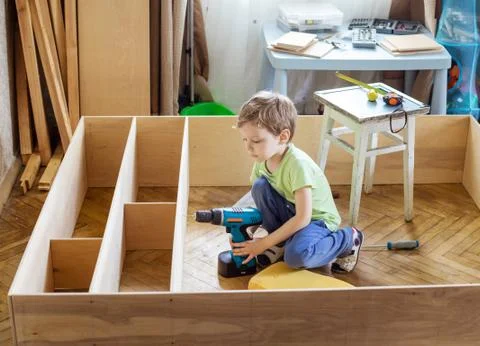 Young boy holding screwdriver while sitting on floor at unfinished shelf unit Foto stock