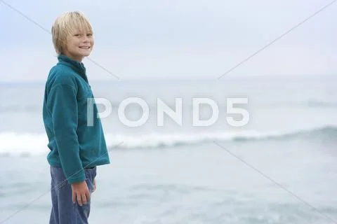 Young Boy On Holiday Standing On Winter Beach Looking Out To Sea Stock Photos