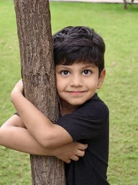 A young boy hugging a tree with a warm smile, symbolizing love for the environme Stock Photos
